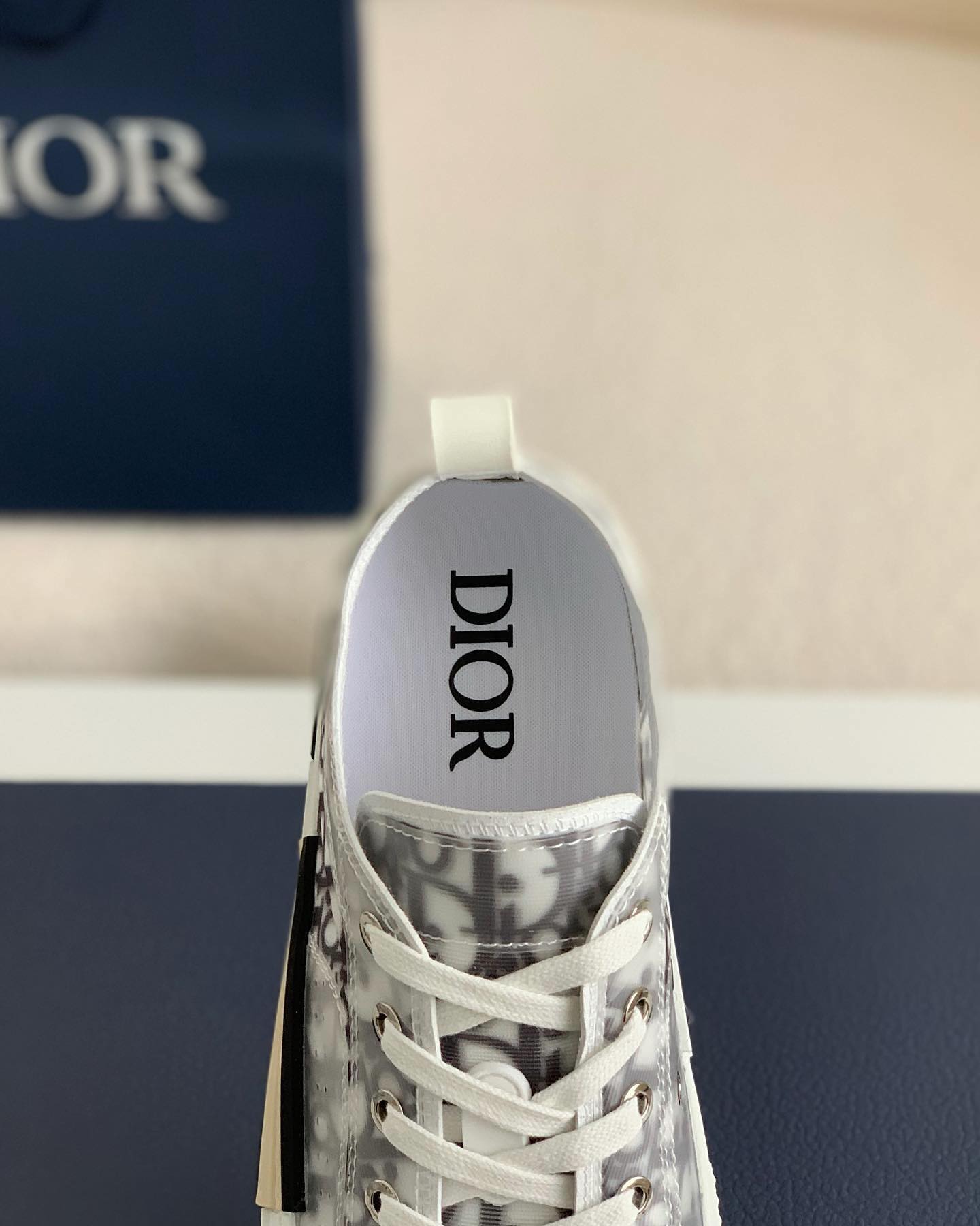 A pair of white Dior B23 High-Top sneakers with a transparent panel showcasing the Dior Oblique jacquard canvas.