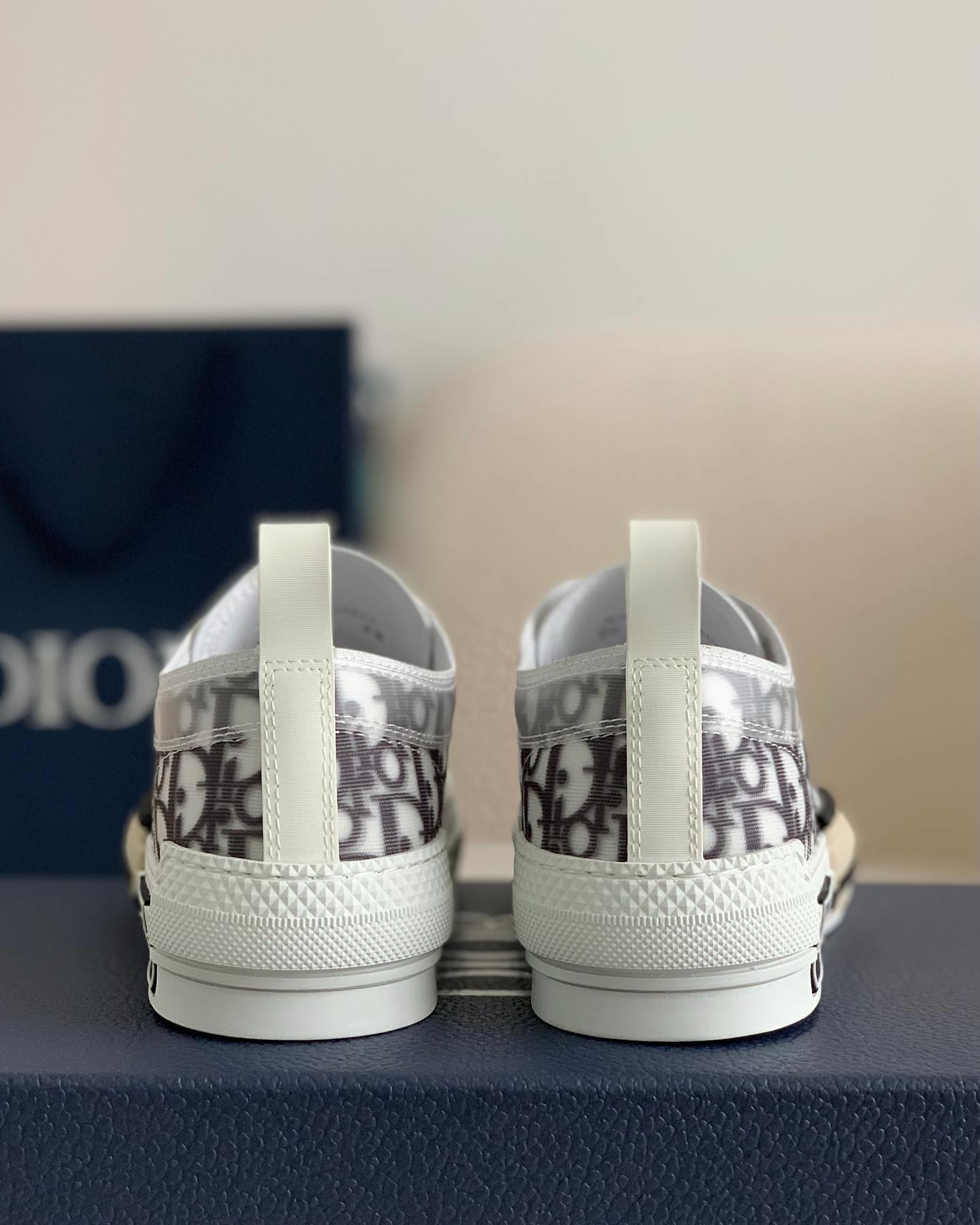 A pair of white Dior B23 High-Top sneakers with a transparent panel showcasing the Dior Oblique jacquard canvas.