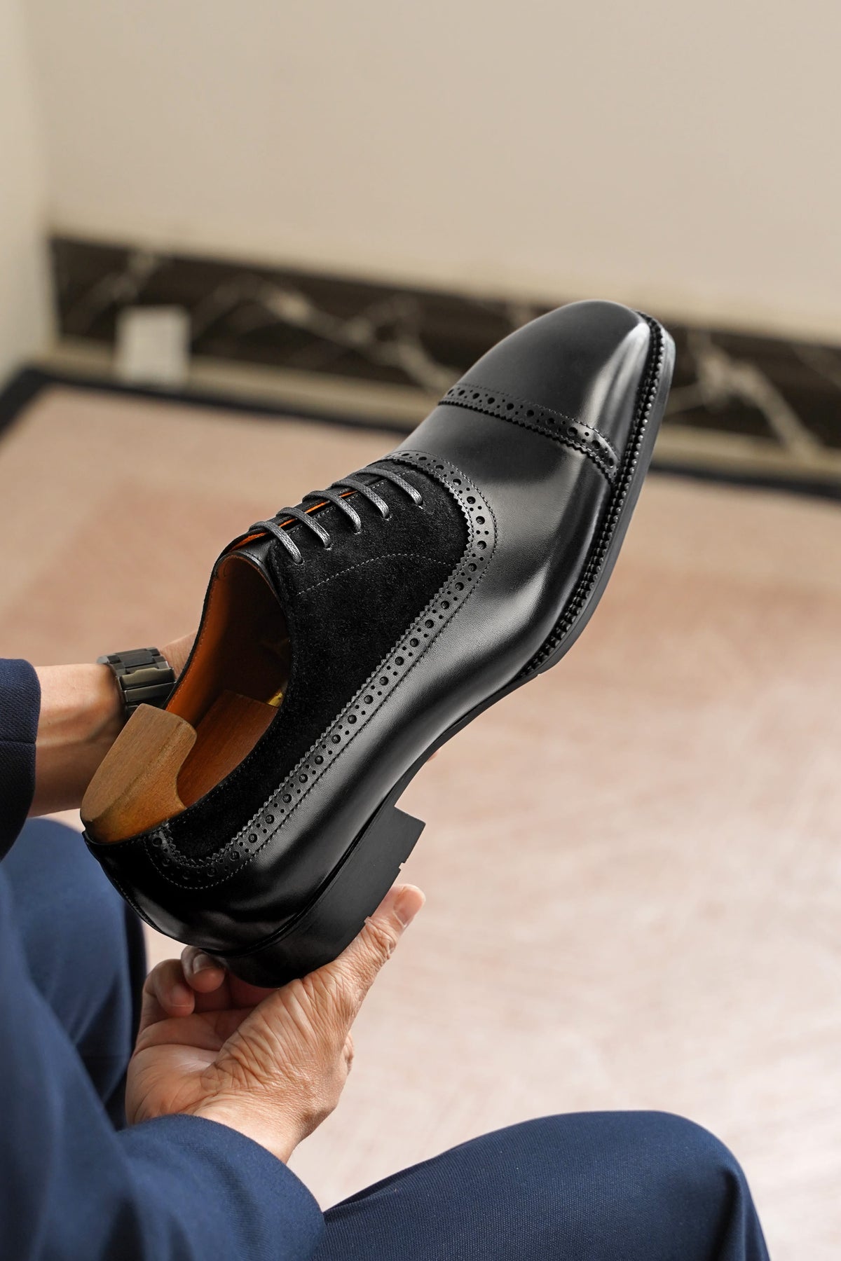 Person holding a black dress shoe with a wooden sole indoors.