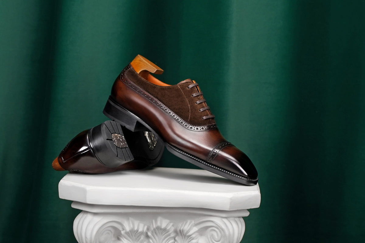 Pair of brown dress shoes on a decorative white pedestal against a green background