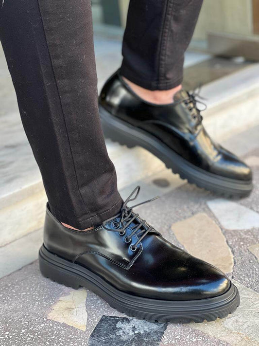 Black Derby Lace-Up Shoes – polished black leather, worn by a man in black trousers with one foot lifted, emphasizing comfort and sleek everyday style.