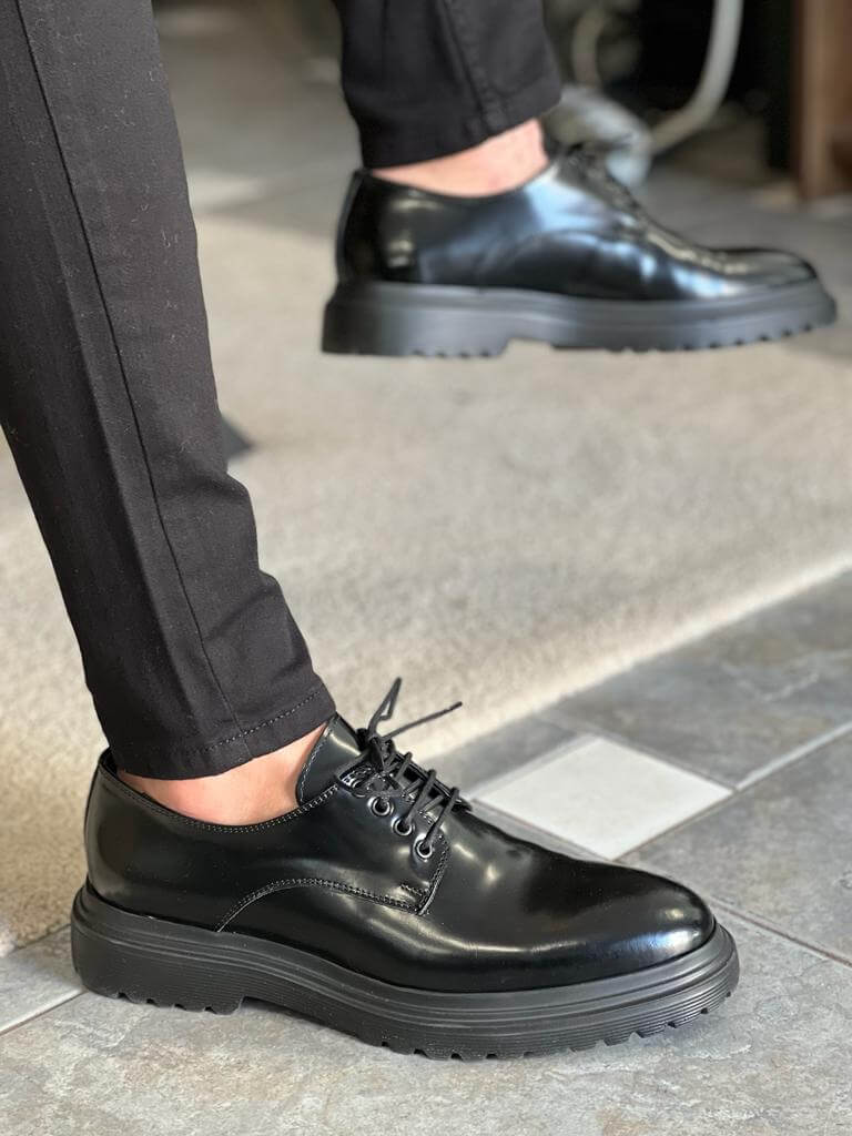 Black Derby Lace-Up Shoes – polished black leather, worn by a man in black trousers, standing on a rug, showcasing sleek design and everyday comfort.