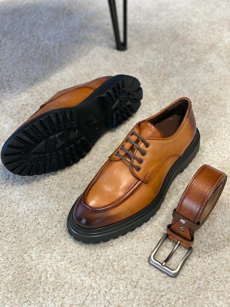 Camel Leather Derby Shoes – one shoe upright and one showing the sole, alongside a matching camel leather belt, for lasting style.