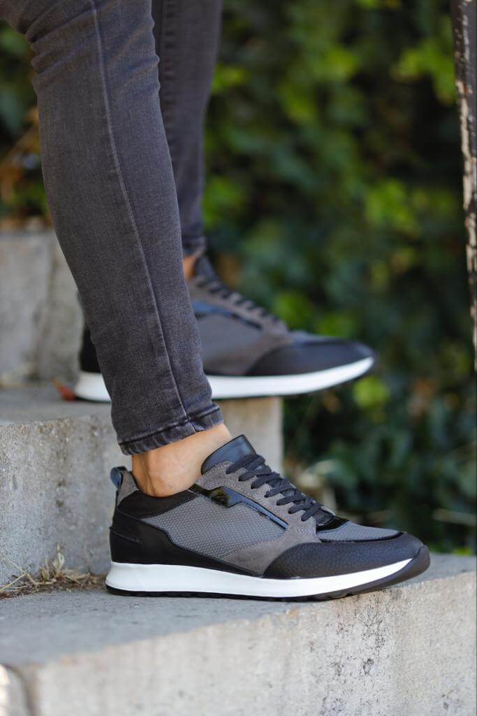 Detailed Gray Sneakers for Casual & Everyday Wear – worn by a man in black jeans, sitting on a wooden bench, showcasing unique detailing and comfort.