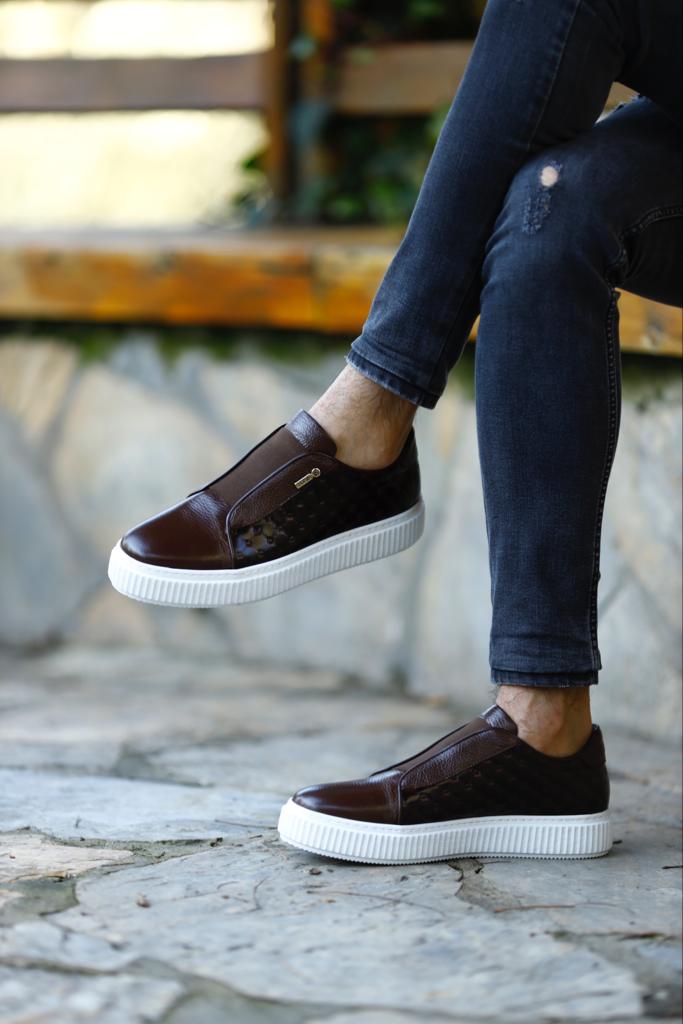 Handcrafted Vortex Brown Float Leather Slip-Ons – worn by a man in black jeans, sitting on a wooden bench, highlighting a durable sole for long-lasting wear.
