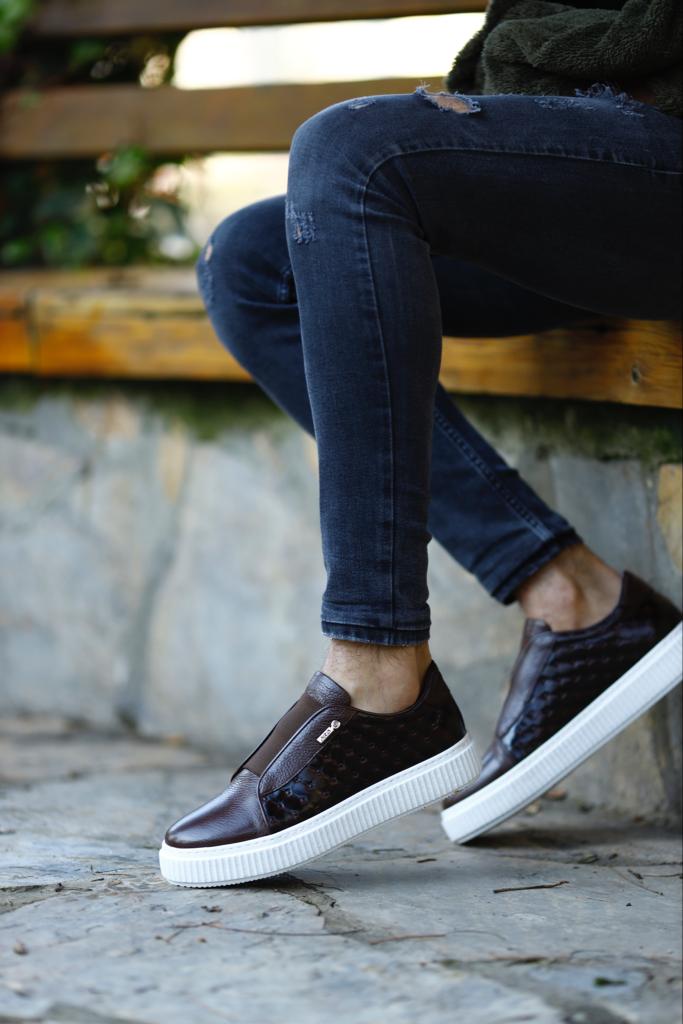 Handcrafted Vortex Brown Float Leather Slip-Ons – worn by a man in black jeans, sitting on a wooden bench, highlighting the durable Eva sole and sleek silhouette.