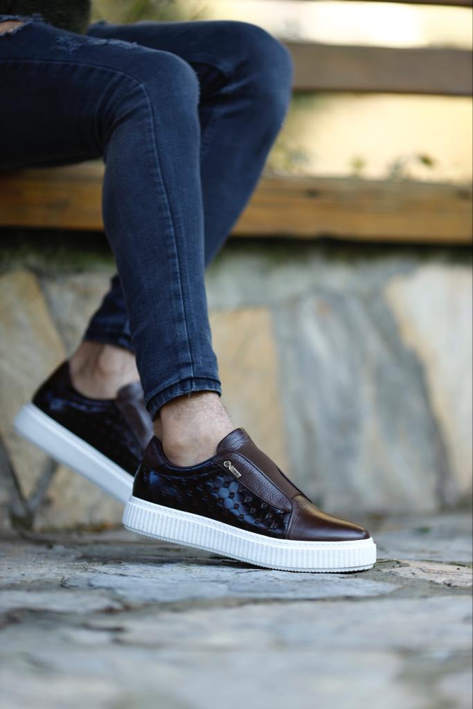 Handcrafted Vortex Brown Float Leather Slip-Ons – worn by a man in black jeans, sitting on a wooden bench, highlighting a durable sole for long-lasting wear.