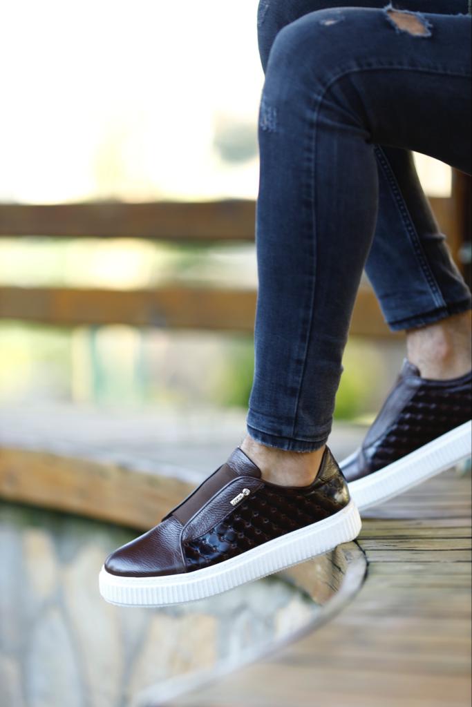 Handcrafted Vortex Brown Float Leather Slip-Ons – worn by a man in black jeans, sitting on a wooden bench, highlighting the durable Eva sole and sleek silhouette.
