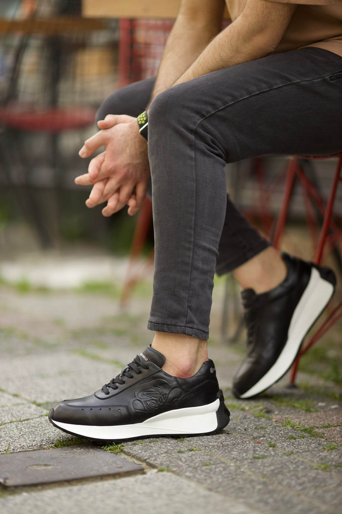 HolloShoe Eva Sole Black Sneakers - Elegant Versatile Footwear – worn by a man in grey jeans, sitting on a red stool, showcasing a sleek design and comfortable fit.