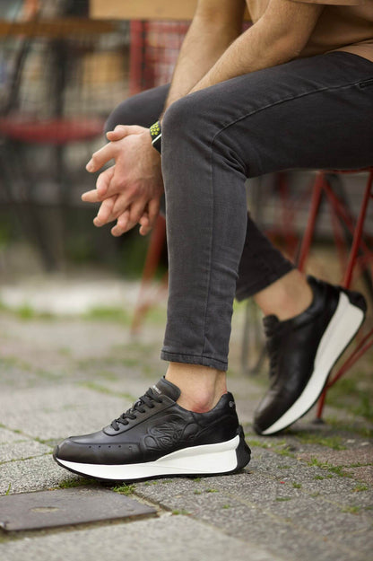 HolloShoe Eva Sole Black Sneakers - Elegant Versatile Footwear – worn by a man in grey jeans, sitting on a red stool, showcasing a sleek design and comfortable fit.