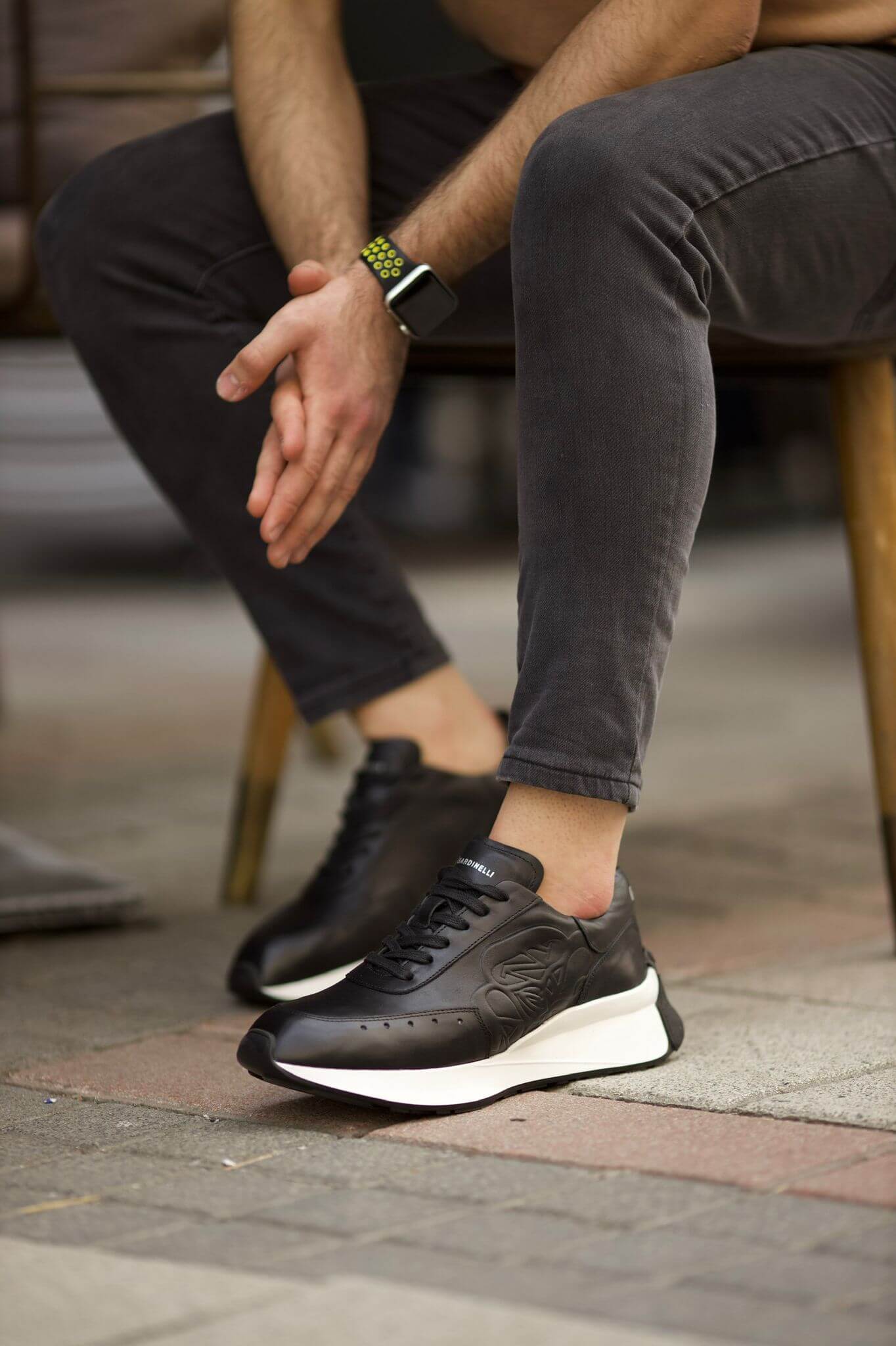 HolloShoe Eva Sole Black Sneakers - Elegant Versatile Footwear – worn by a man in grey jeans, sitting, with hands on his knees, highlighting premium comfort.