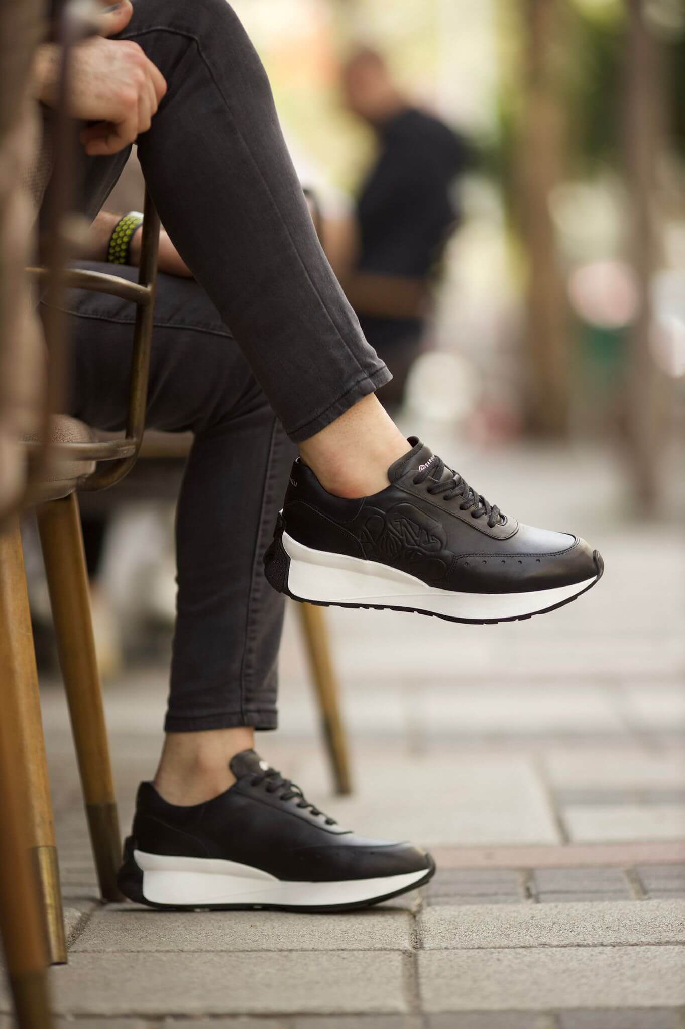 HolloShoe Eva Sole Black Sneakers - Elegant Versatile Footwear – worn by a man in grey jeans, with one foot elevated, highlighting the sleek design and a chunky sole.