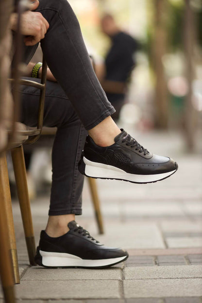 HolloShoe Eva Sole Black Sneakers - Elegant Versatile Footwear – worn by a man in grey jeans, with one foot elevated, highlighting the sleek design and a chunky sole.