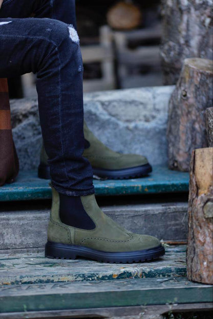 HolloShoe Khaki Nubuck Wingtip Chelsea Boots for All-Day Comfort – a man wearing the khaki nubuck boots with distressed denim and one foot resting on a log, showing the tread.