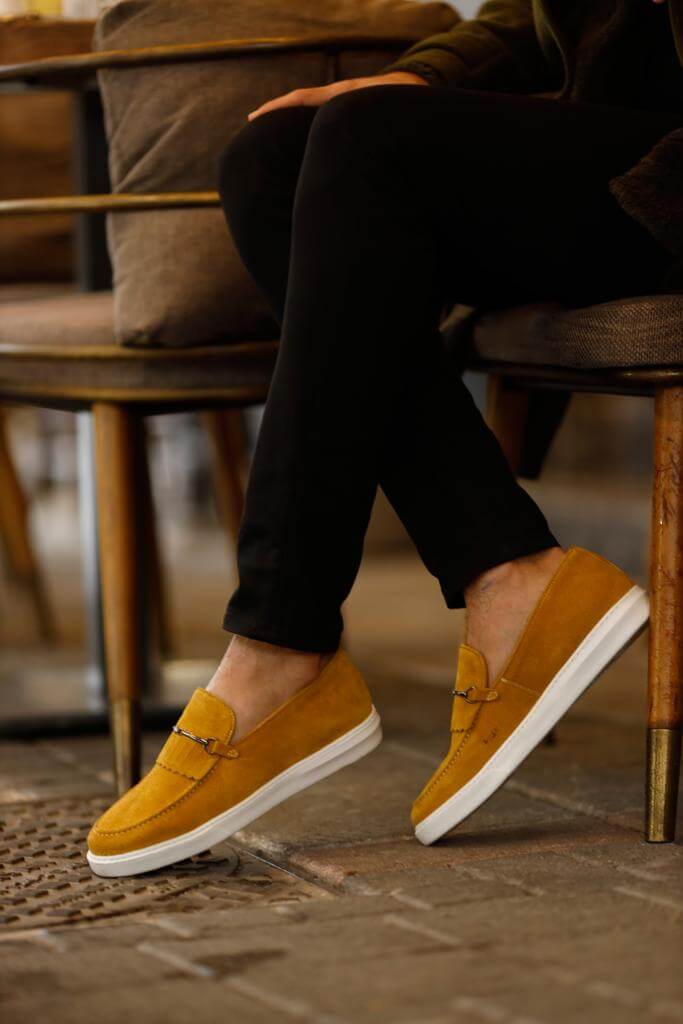 HolloShoe Special Edition Iron Detailed Yellow Slip-Ons – worn by a man in black trousers, sitting in a chair, showcasing a vibrant yellow hue and a comfortable fit.