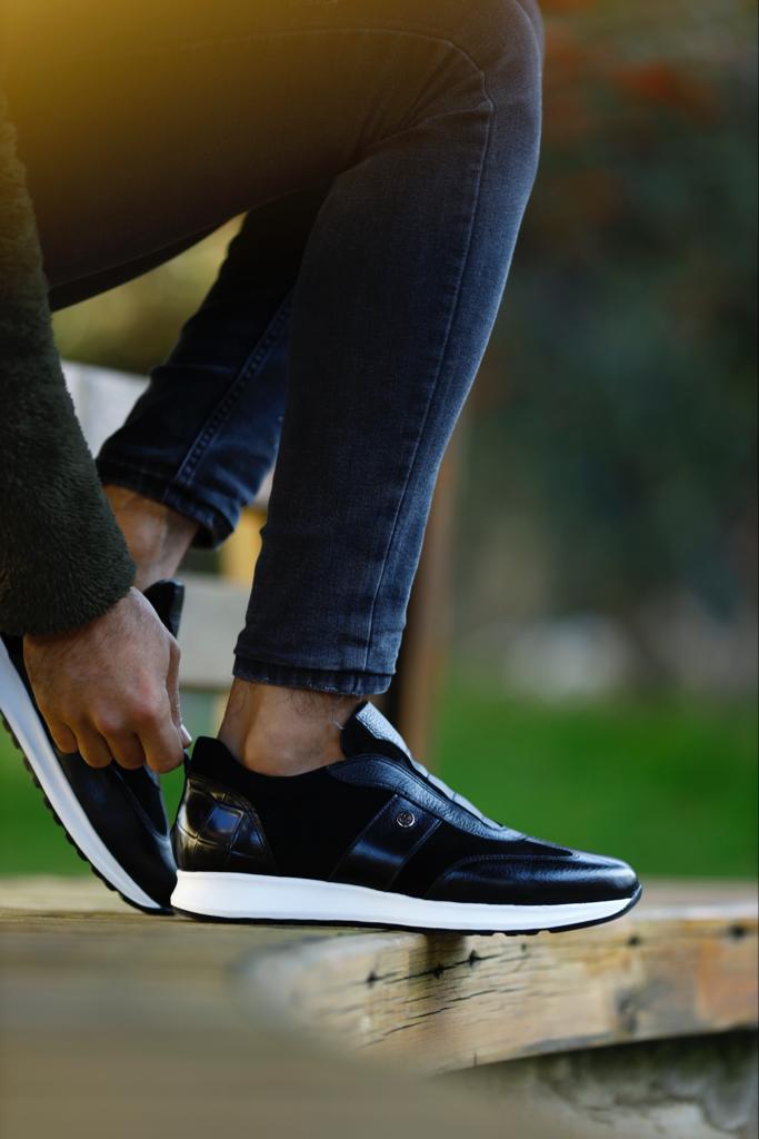 Modern Black Suede Leather Sneakers – worn with black jeans, tying laces on a wooden bench, showcasing a sleek design and comfortable fit.