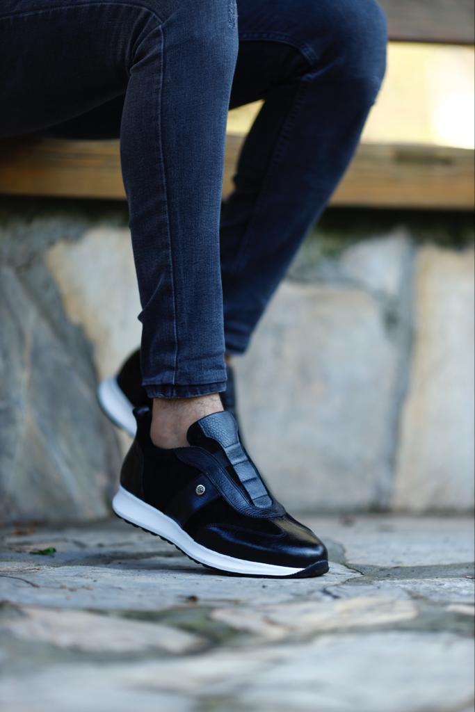 Modern Black Suede Leather Sneakers – worn by a man in black jeans, with one foot elevated, showcasing the sleek design and a modern blend of materials.