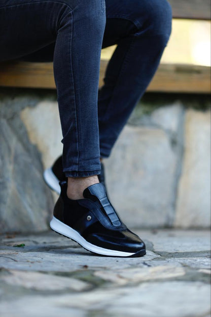 Modern Black Suede Leather Sneakers – worn by a man in black jeans, with one foot elevated, showcasing the sleek design and a modern blend of materials.