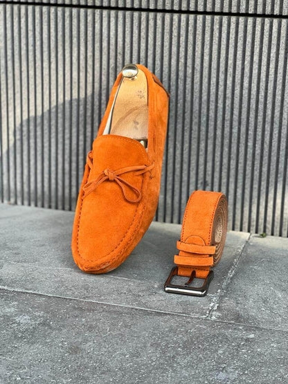 Premium Oakmond Orange Suede Driving Loafers – one shoe upright and a matching belt on a grey concrete floor, highlighting a luxurious touch and an elegant design.