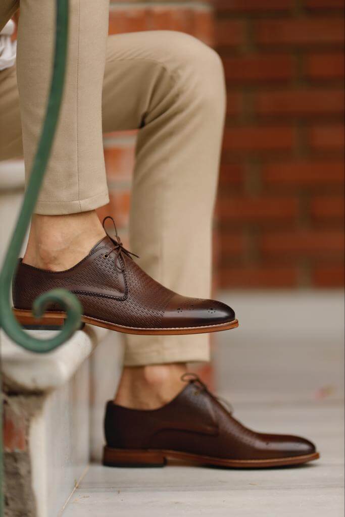 Unique Design Brown Leather Lace-Up Shoes – worn by a man in beige chinos, with one foot lifted, showcasing the unique leather pattern and lightweight soles.